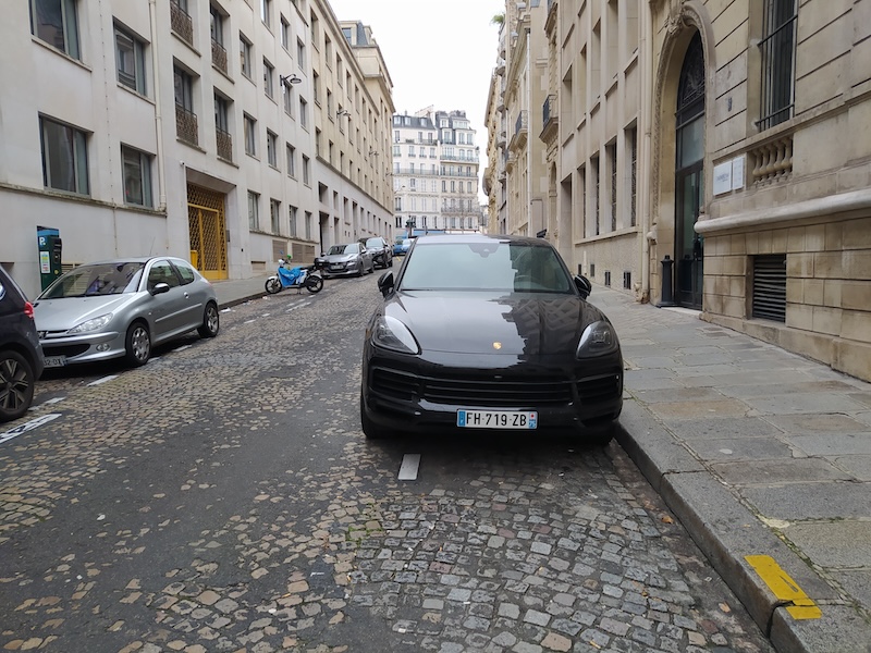 An SUV overhanging a parking space on a narrow paved road