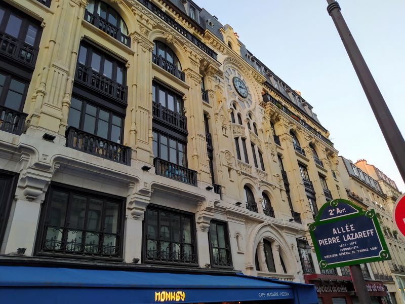 Neogothic façade featuring church-style windows spanning multiple storeys, carved faces and animals, and a colourful clock surrounded by signs of the zodiac