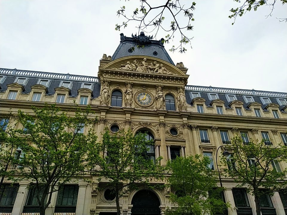 Grand stone façade. The central tower features a number of statues and a gold-handed clock with Roman numerals