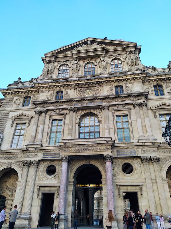 The Pavillon Sully, as seen from the Cour Napoléon. Columns and statues adorn this façade, along with a golden-handed clock
