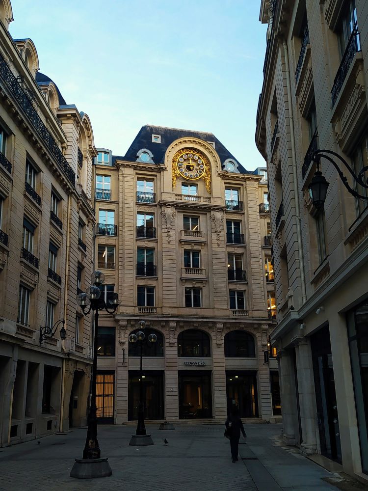 A photo looking along a pedestrianised street to a stone facade with a large golden clock