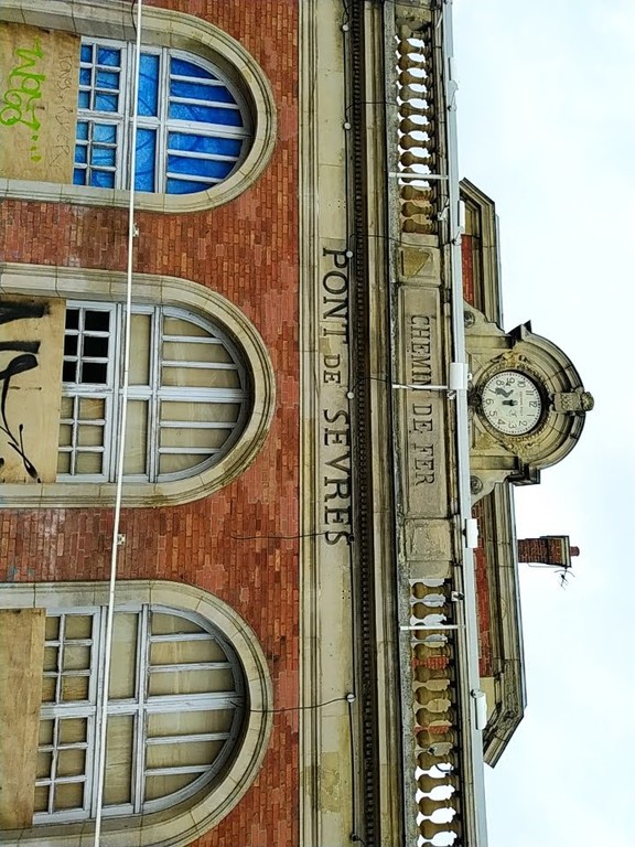 Boarded-up railway station building. Text engraved in wall: CHEMIN DE FER : PONT DE SEVRES