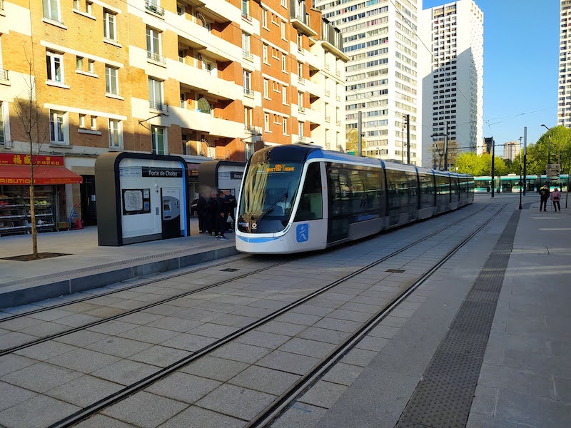 Tram at Porte de Choisy station. Behind is another tram. There are tall brick and concrete buildings in the background