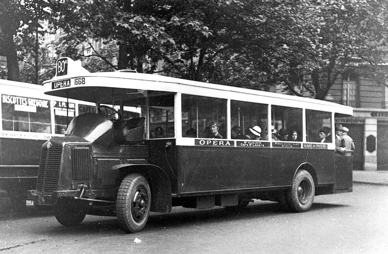 Bus full of passengers, both inside and on an open area at the rear. The bus is labelled BO. Its destination is marked as Opéra; it also stops at Saint-Augustin, Gare Saint-Lazare, Place Victor Hugo, Étoile, and the Gare de Passy.